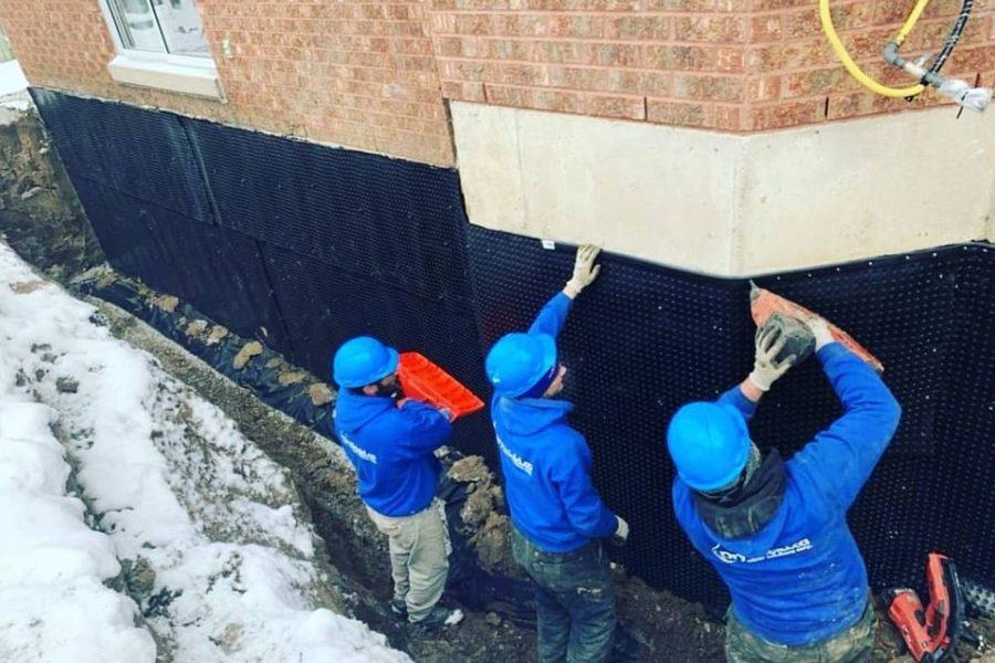 Workers applying drainage membrane to foundation